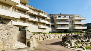 A multi-story residential building with balconies, a stone wall, and a paved entrance. - Les Jardins de Quatrina 2 bedrooms sea view (PROPRIANO)