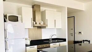 A modern kitchen with white cabinetry, a black countertop, and stainless steel appliances. - Les Jardins de Quatrina 2 bedrooms sea view (PROPRIANO)