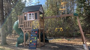 Une structure de jeu en bois, dotée d’un toboggan et d’échelles d’escalade, installée dans un espace boisé.