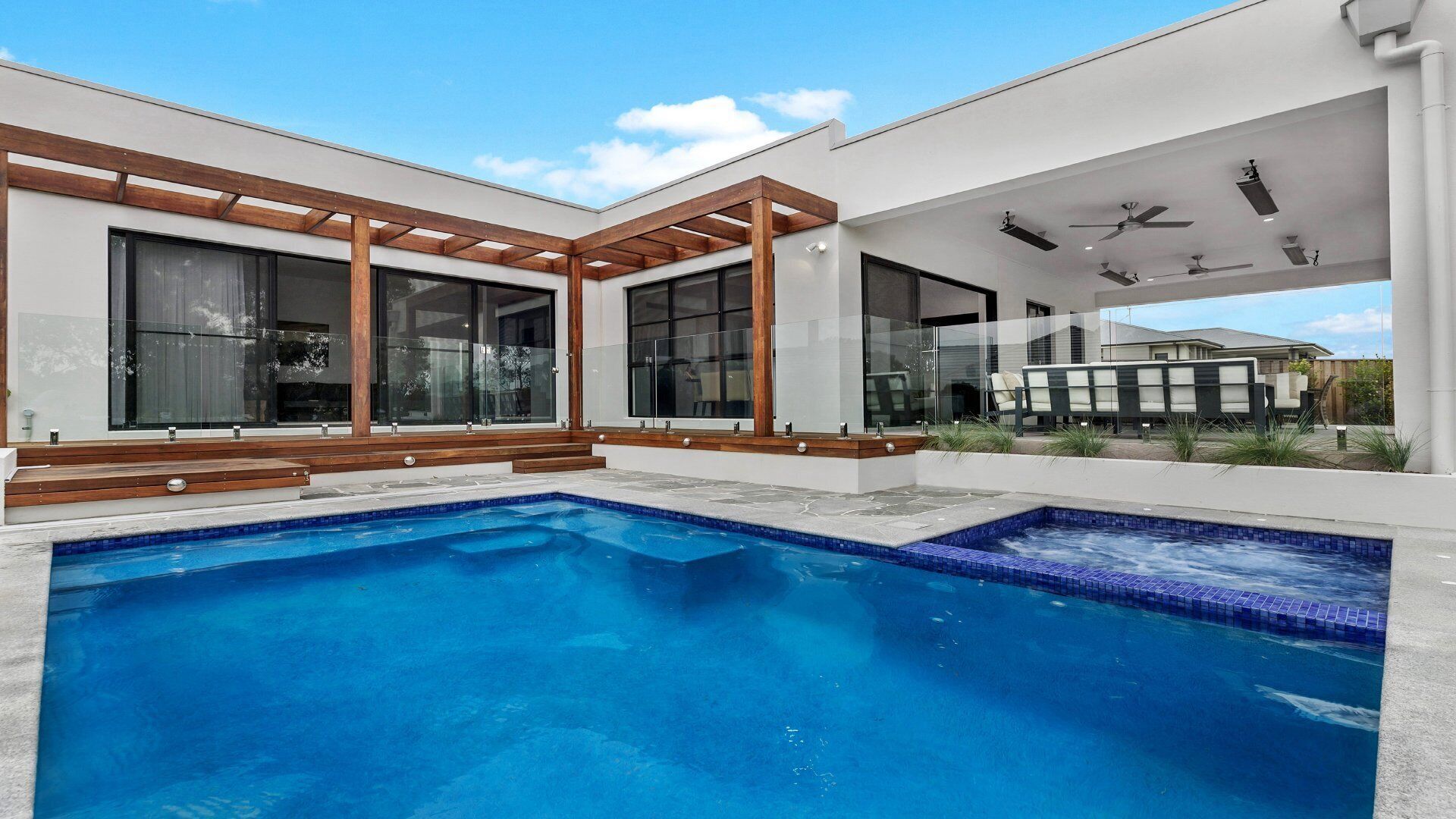 Una casa moderna amb piscina, grans finestres i una zona exterior coberta.