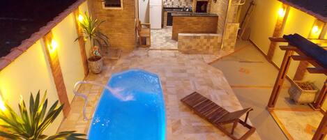 A swimming pool with a wooden deck, a small bar area, and potted plants.