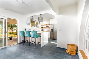 Een moderne keuken met een centraal eiland, barkrukken en een koelkast.