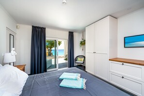 Een hotelkamer met een bed, een bureau, een stoel, een televisie en uitzicht op het strand.