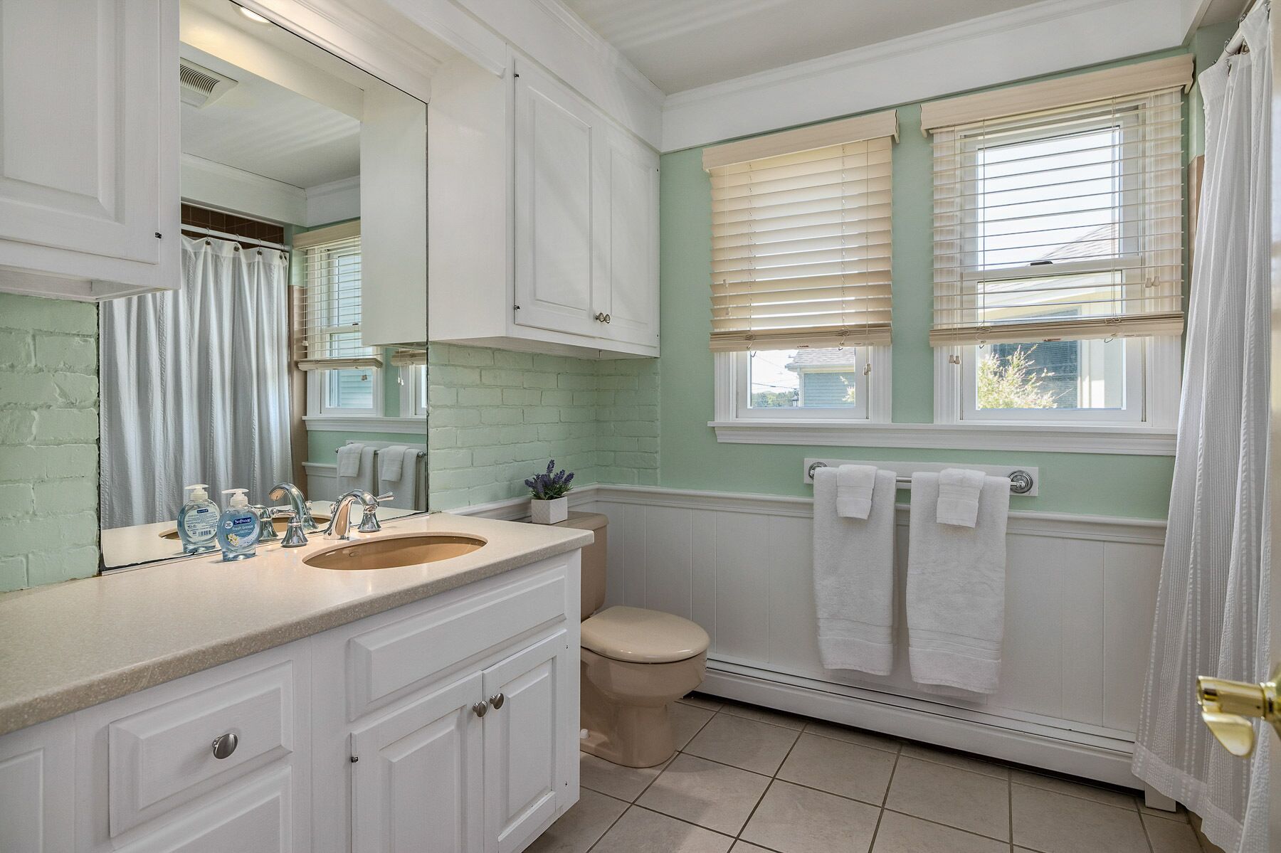 A bathroom with a double sink, a toilet, and a window with blinds.