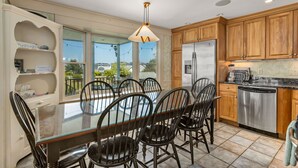A modern kitchen with a dining area, featuring a glass table, wooden cabinets, and stainless steel appliances. - Spacious Beach Villa - Ocean Views - 3 Minute Walk to Shore - Available All Year (Wells)