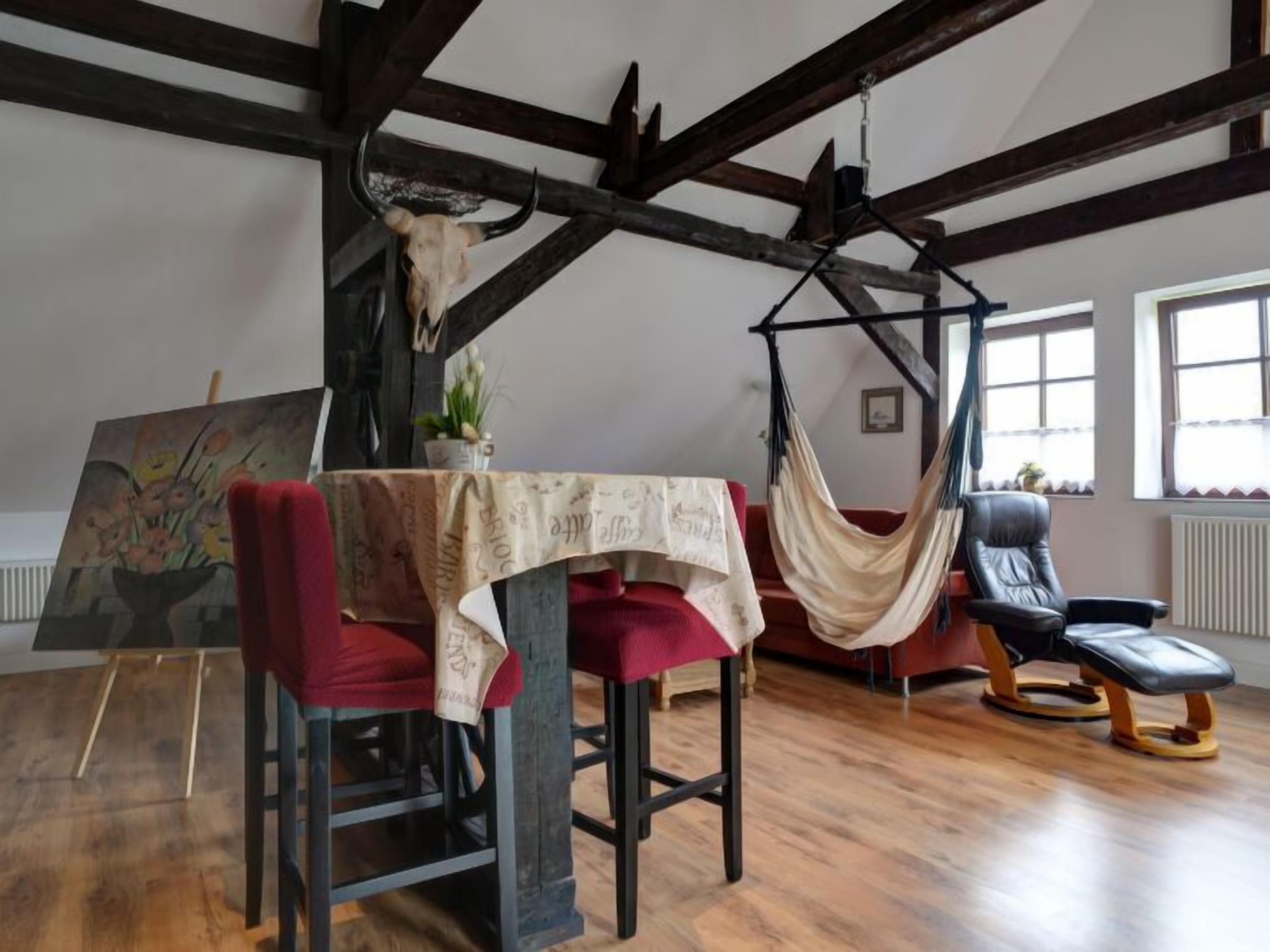 A room with a hammock, a painting, and a table with a red chair.