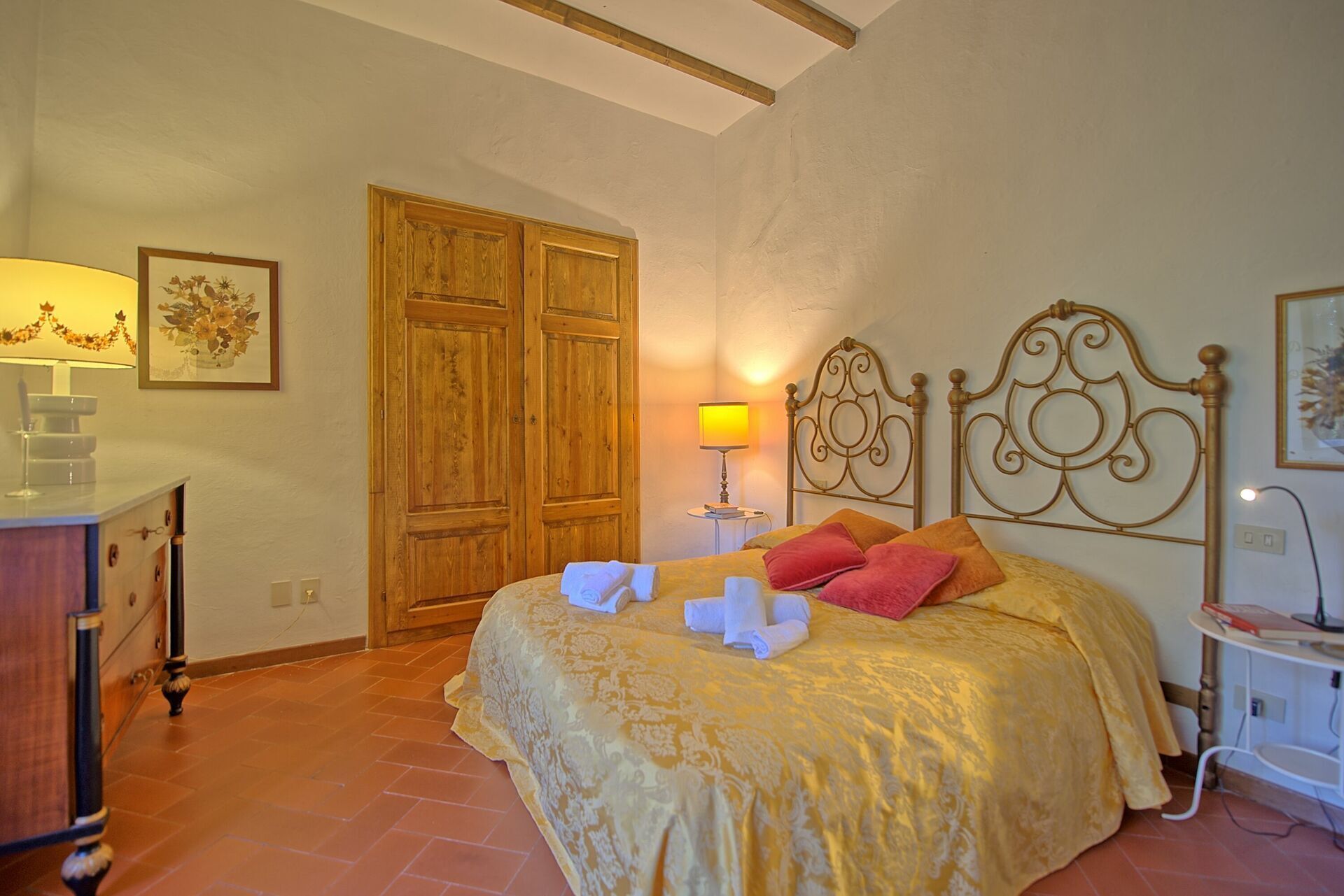 Quarto com cama, guarda-roupa de madeira, abajur e uma pequena mesa.