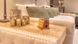 Une table en bois, bien rangée et agrémentée d’objets décoratifs, un lit avec des oreillers et une lampe dans une pièce chaleureuse.