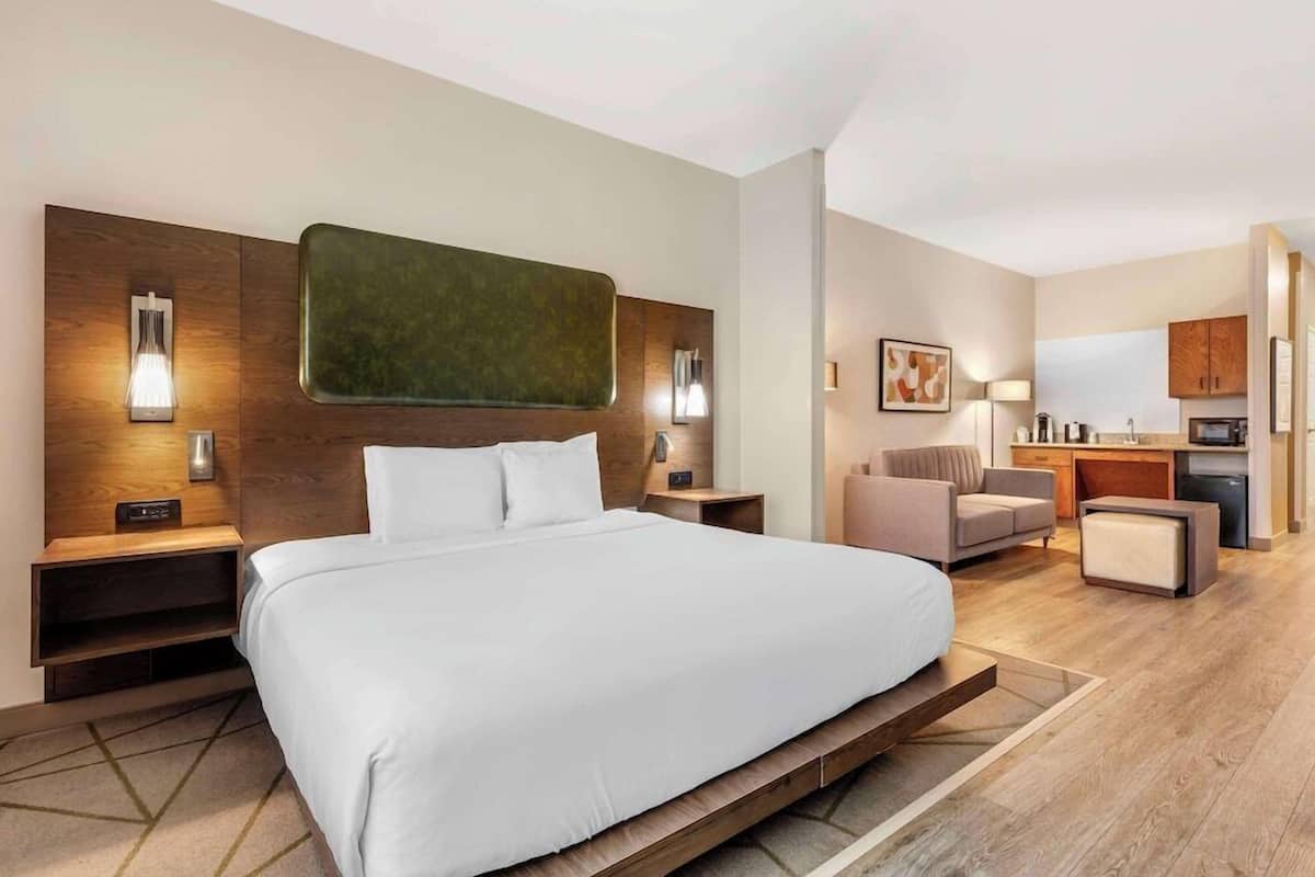 Une chambre d’hôtel moderne équipée d’un grand lit, de tables de chevet, d’un bureau, d’une chaise et d’une kitchenette.