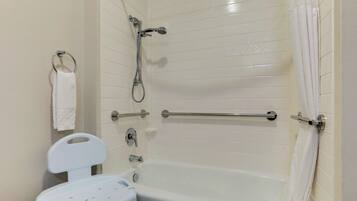 A bathroom with a bathtub, a showerhead, a toilet, and a grab bar.