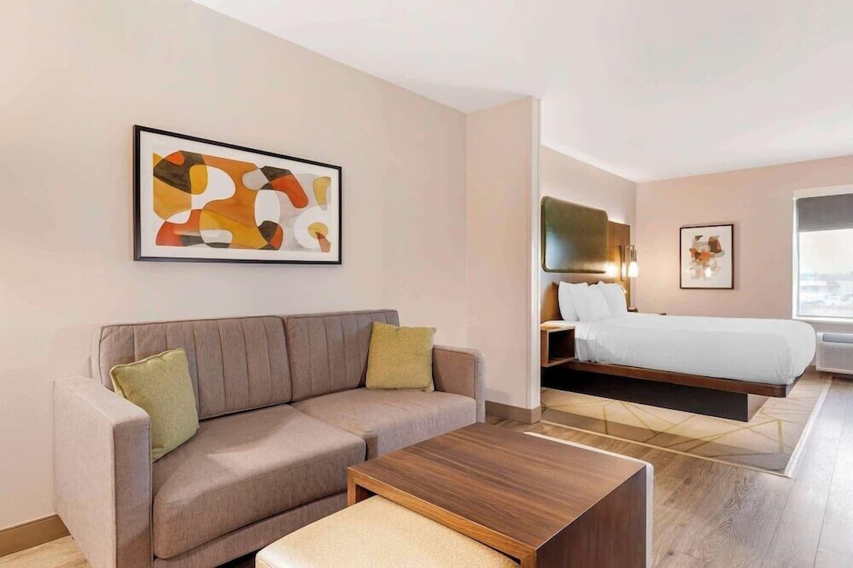 Une chambre d’hôtel moderne avec un canapé, une table basse en bois, un lit et un téléviseur.