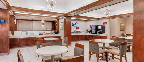 Un área de café amplia con mesas y sillas redondas, detalles de madera y un mostrador visible con una máquina de café.