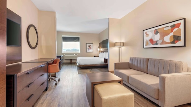 Ein Hotelzimmer mit einem Bett, einem Sofa, einem Schreibtisch mit Schubladen, einem Fernseher, einer Lampe und einem gerahmten Bild an der Wand.