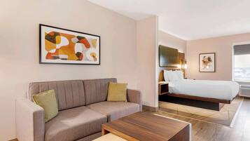 Une chambre d’hôtel moderne, dotée d’un canapé, d’un lit, d’une table basse en bois et d’un grand tableau abstrait accroché au mur.