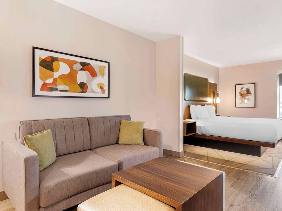 Une chambre d’hôtel moderne, dotée d’un canapé, d’un lit, d’une table basse en bois et d’un grand tableau abstrait accroché au mur.