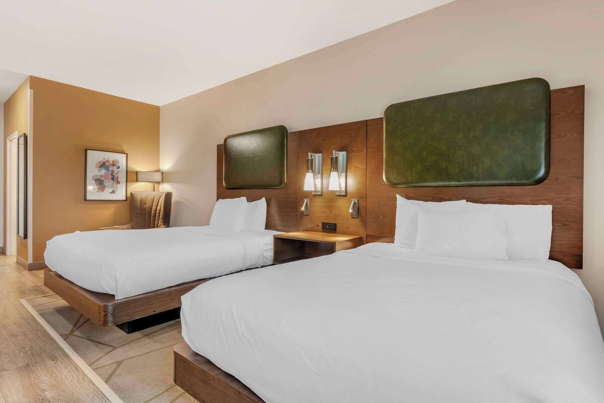 Une chambre d’hôtel avec deux lits simples, des têtes de lit en bois, une table de chevet avec une lampe et un tableau encadré au mur.