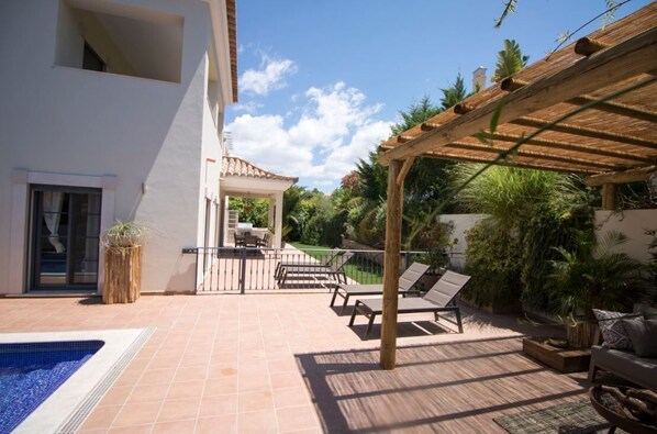 Un patio con piscina, mobiliario exterior y una pérgola.