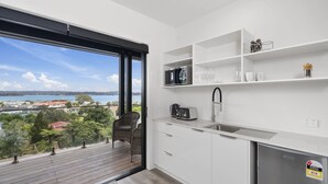 Una cocina moderna con un ventanal grande, armarios blancos y vistas al paisaje costero.