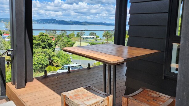 Una terraza de madera con una mesa y dos sillas, con vista a un paisaje que incluye agua y vegetación.