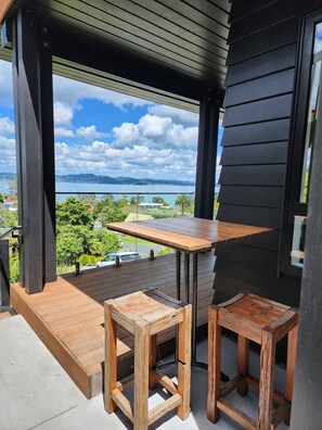 A wooden deck with a table and two chairs, overlooking a scenic view of a body of water and greenery.