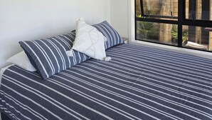 Un dormitorio con una cama grande, un cartel de playa enmarcado, un equipo de aire acondicionado y una ventana con vista a una estructura de madera.