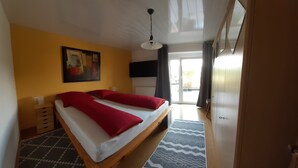 A bedroom with a bed, a painting on the wall, a television, and a view of the outdoors.