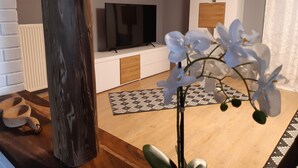 A living room with a TV, white furniture, a patterned rug, and an orchid plant.