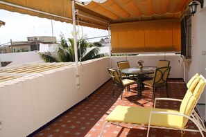 A covered outdoor area with a round table and chairs, a small table with a vase, and a yellow lounge chair. - Lovely apartment for 4 guests with A/C, WIFI, TV and terrace (Chipiona)