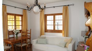 Een kamer met een witte bank, een houten eettafel, stoelen en een kroonluchter.