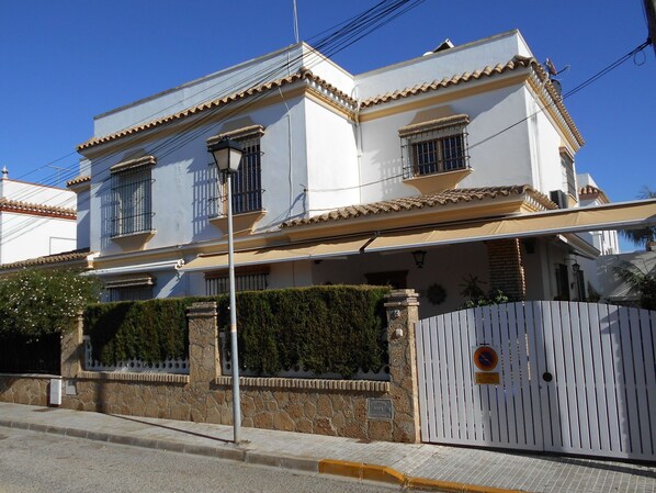 A two-story building with a white facade, a tiled roof, and a gated entrance. - Lovely apartment for 4 guests with A/C, WIFI, TV and terrace (Chipiona)