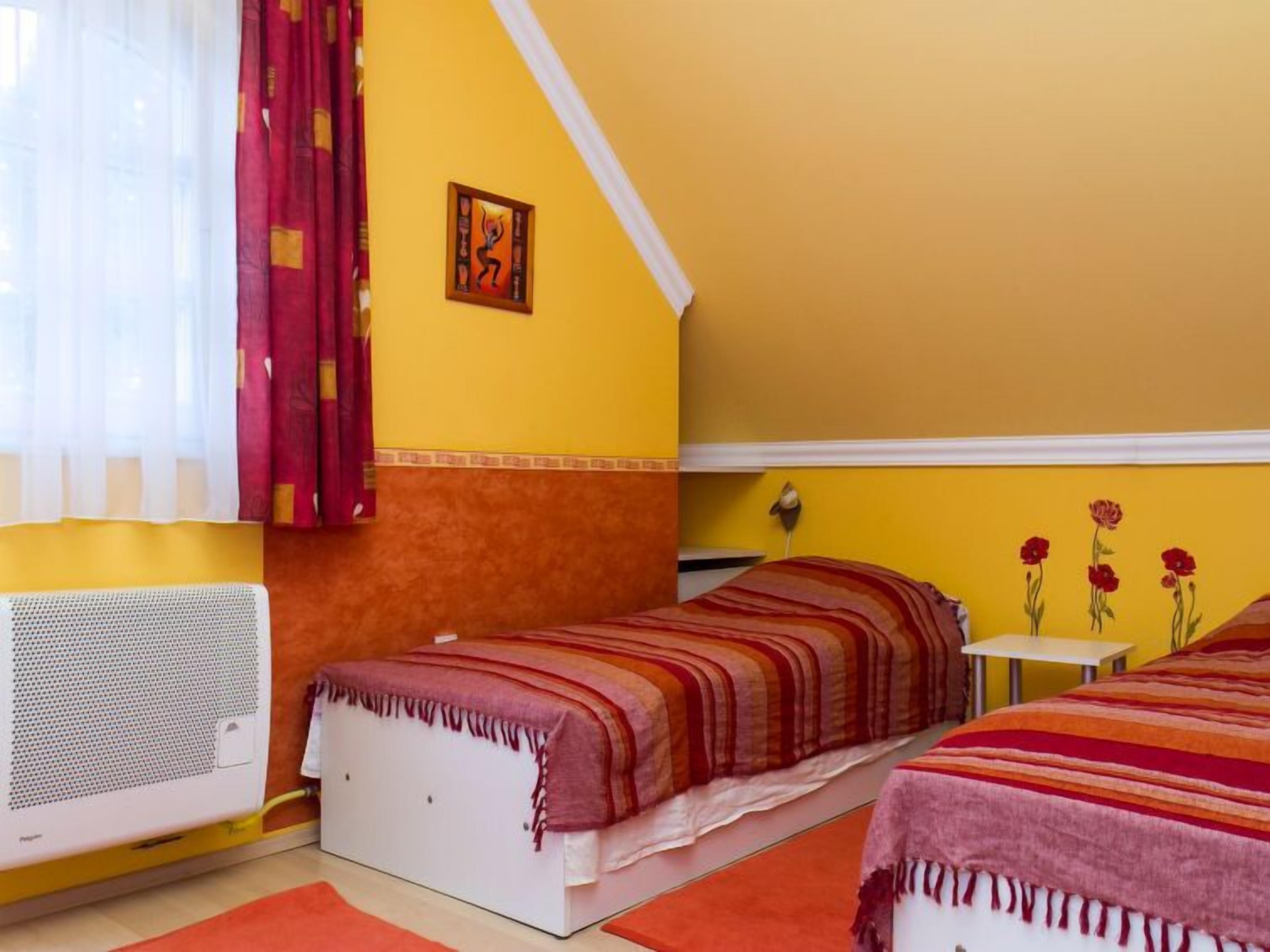 Een kamer met twee bedden, een verwarming, een kleine tafel en een muur met een schilderij.