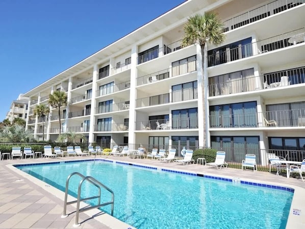 Um hotel com vários andares e área de piscina, incluindo piscina, espreguiçadeiras e uma palmeira.