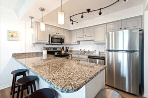 A kitchen with granite countertops, stainless steel appliances, and pendant lighting.