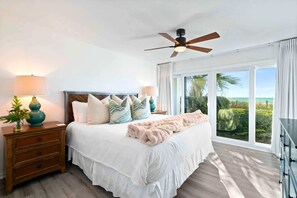 A bedroom with a bed, nightstands, a ceiling fan, and a large window with a view.