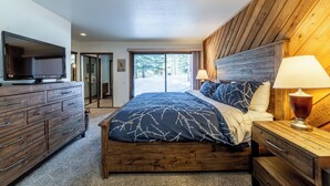 Un dormitorio con una cama grande, cabecera de madera, un televisor en una cómoda y vistas al exterior.
