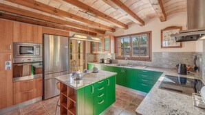Una cocina con vigas de madera, electrodomésticos de acero inoxidable, armarios verdes y un ventanal amplio.