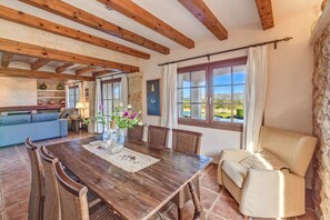 Un coin repas avec une table en bois, des chaises, un vase de fleurs et une vue sur l’extérieur.