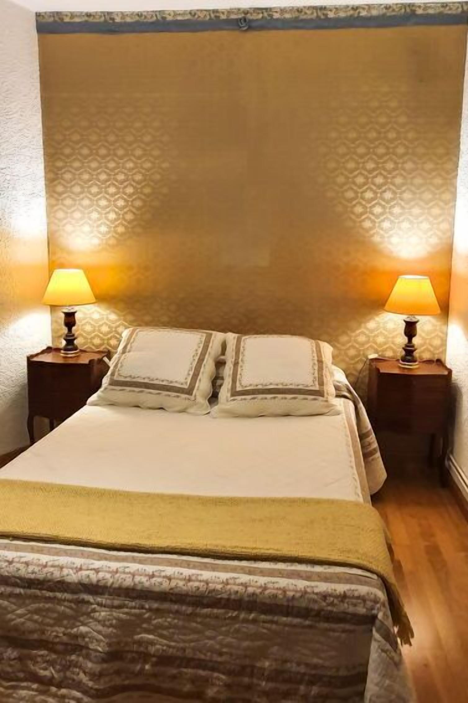 A hotel room with a bed, two bedside lamps, and a patterned wall.