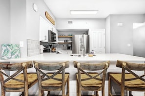 Una cocina moderna con armarios blancos, una isla central y sillas de madera.