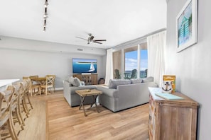 Una sala de estar moderna con sofá, mesa de comedor, sillas, televisor y vista al mar.