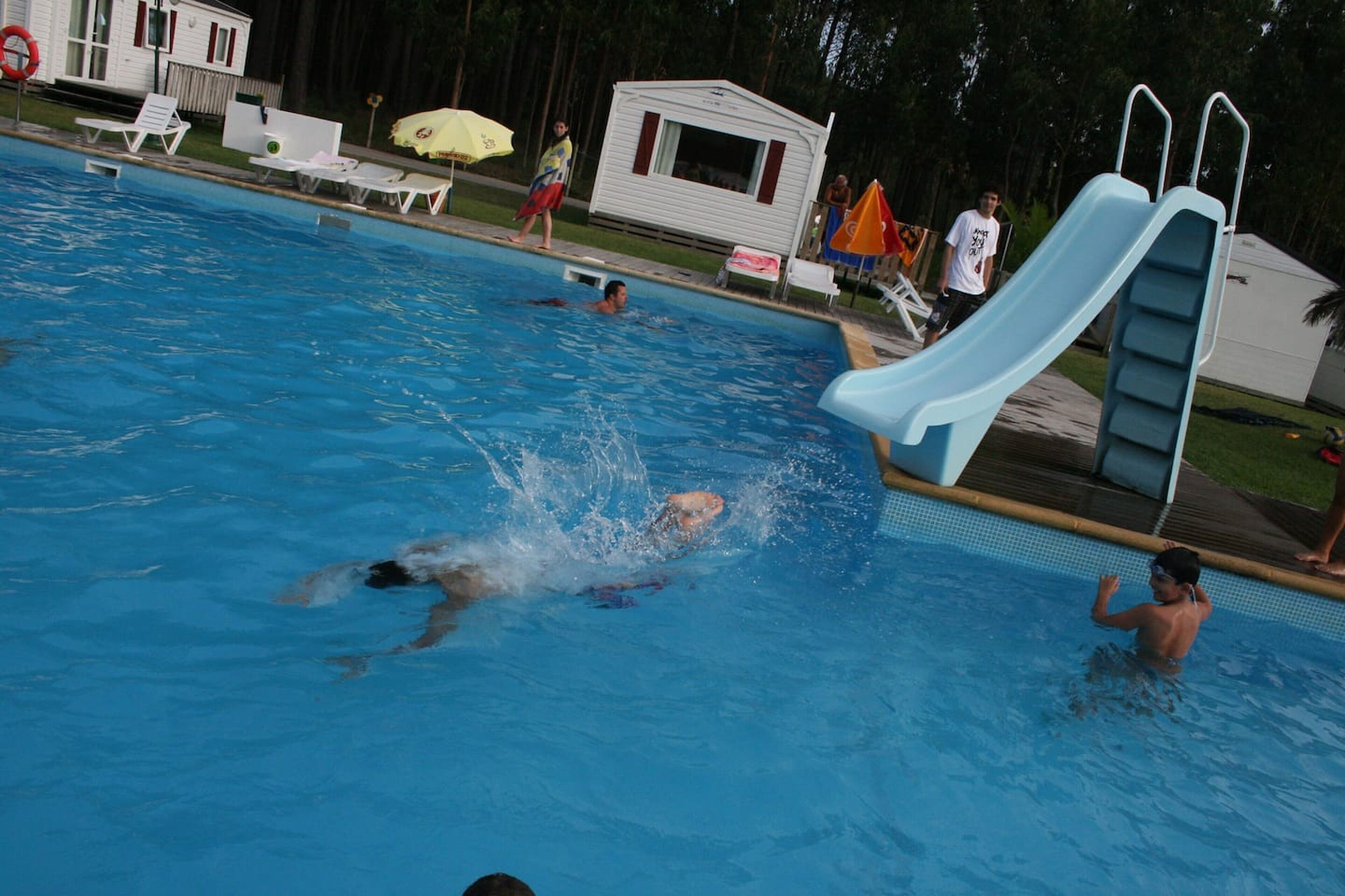 A swimming pool with a slide, lounge chairs, and a small cabin.