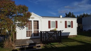 A white mobile home with red shutters, a wooden deck, and a small garden area. - Landshause Bungalow T2 13A (Pataias)