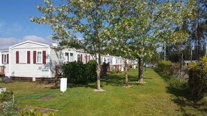 A row of white mobile homes with red shutters, surrounded by green grass and trees. - Landshause Bungalow T2 13A (Pataias)