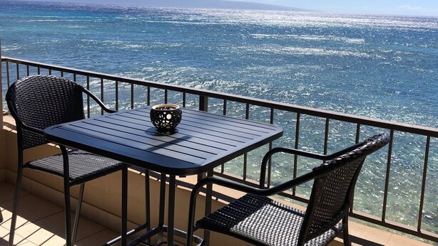 Un balcón con una mesa y dos sillas, con vista a una masa de agua y una tierra distante.