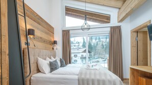 Ein Schlafzimmer mit einem großen Bett, einem Holz-Kopfteil, einem Fenster mit Vorhängen, einer Pendelleuchte und einem Holzkasten.