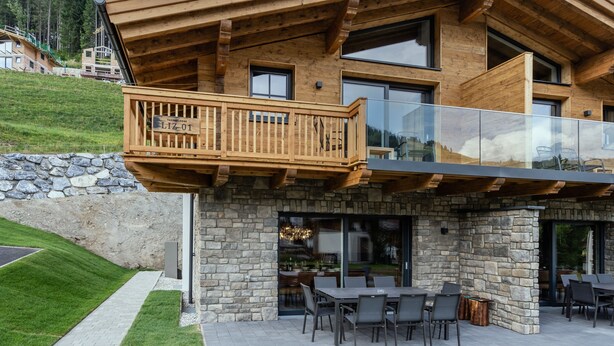 Ein modernes Gebäude mit einer Stein-Fassade, einem Holzbalkon und einem Glasgeländer.