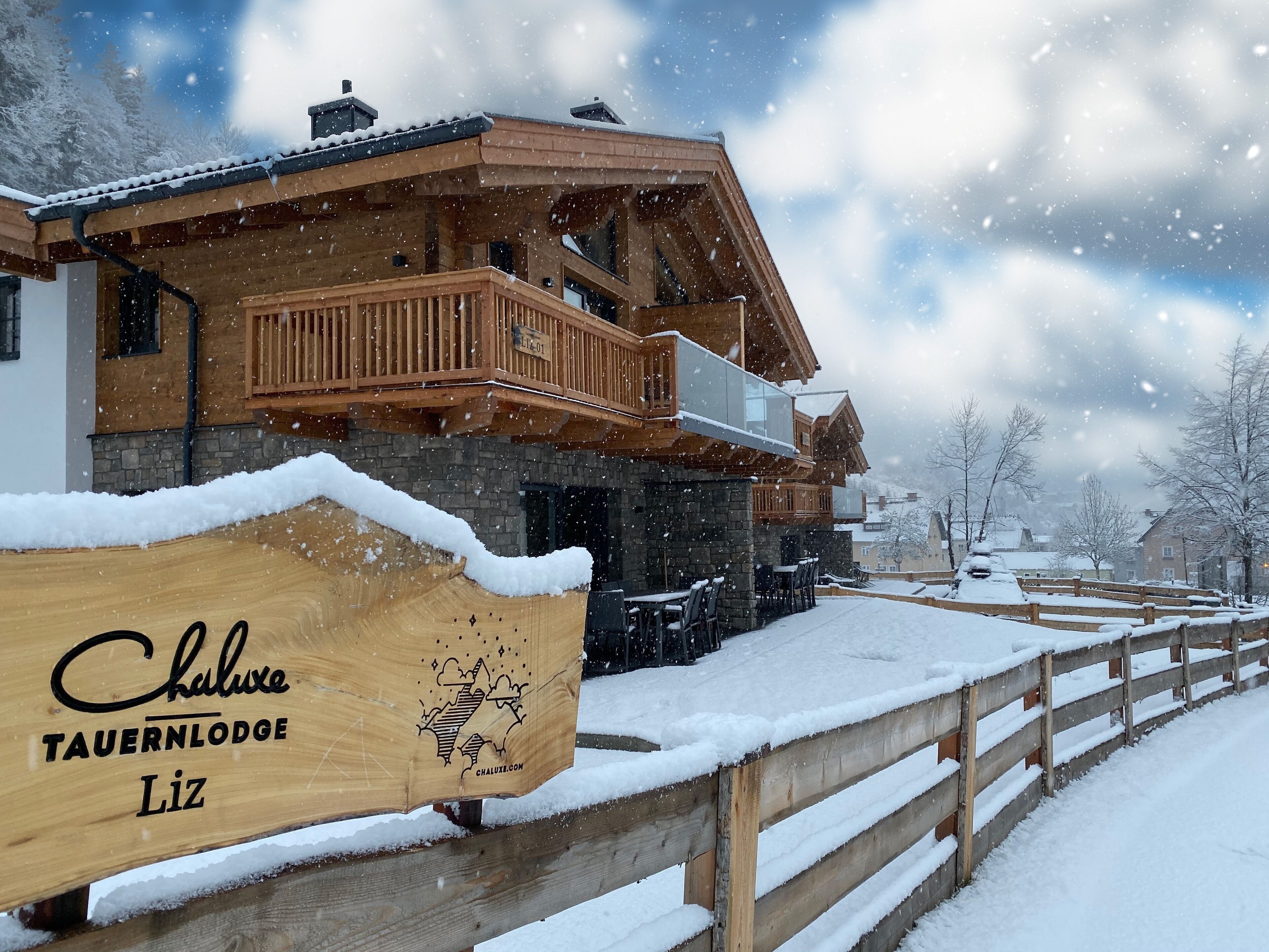 Un chalet en bois doté d’un balcon, entouré d’arbres couverts de neige et d’une clôture en bois.