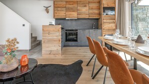 Eine moderne Küche mit Holzschränken, einer Steinwand und einem Essbereich mit Teppich in Schwarz und Stühlen in Orange.