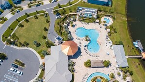 Een luchtbeeld van een resort met een groot centraal zwembad, meerdere kleinere zwembaden en een strand met ligbedden.