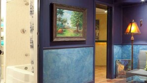 A room with a bathtub, a framed painting of a tropical scene, and a lamp. - DuPont - Scandinavian Café & Garden Apartment (Washington)